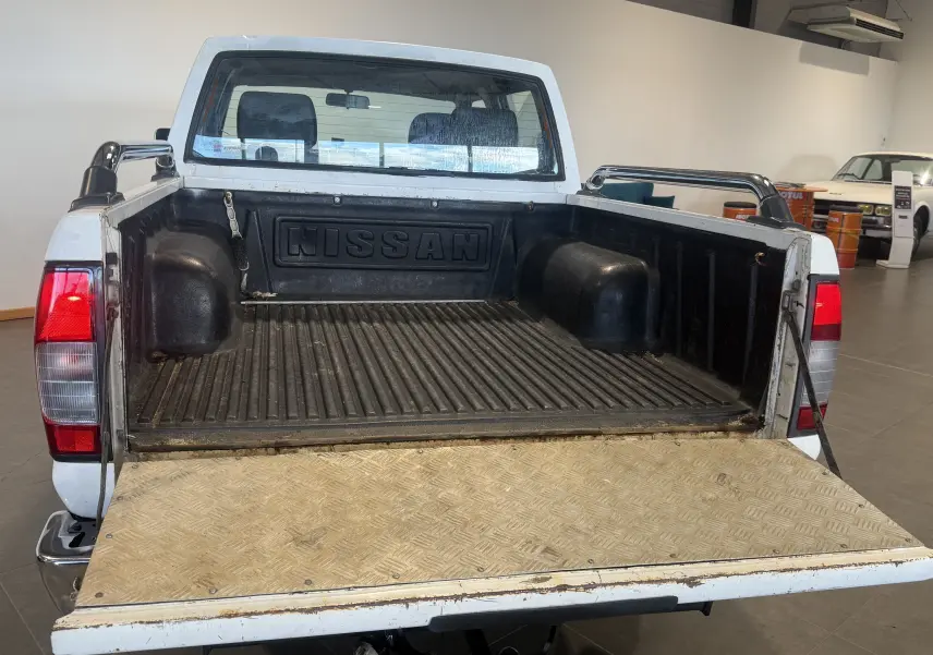 Vue arrière du Nissan Navara NP300 blanc de 2002, plateau ouvert avec benne noire et ridelle abaissée en métal.
