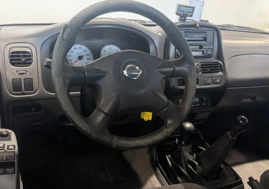 Vue intérieure du tableau de bord et volant usé du Nissan Navara NP300 2002 avec boîte manuelle et commandes centrales visibles.