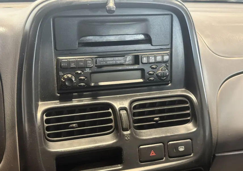 Gros plan sur la console centrale noire du Nissan Navara NP300 2002 avec autoradio et commandes d’aération visibles.