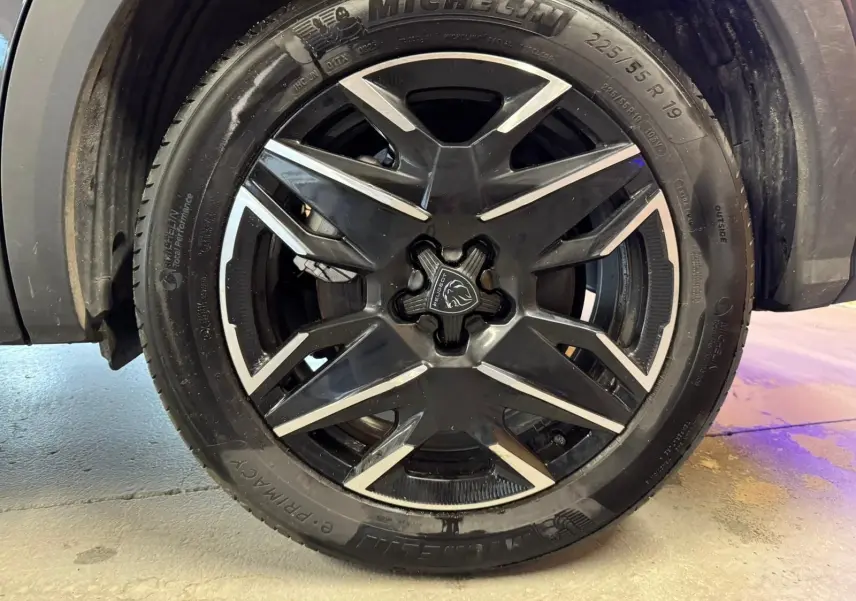 Gros plan sur la jante noire et argentée du Peugeot 5008 gris, mettant en valeur le logo lion au centre.