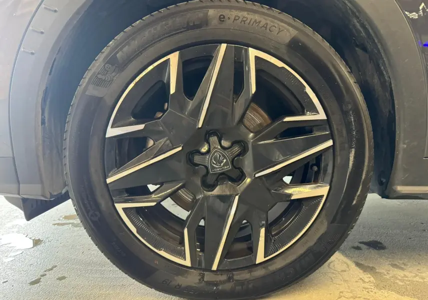 Gros plan sur la roue avant gauche du Peugeot 5008 gris 1.2 HYBRID 136 GT avec jante alliage noire et argent.