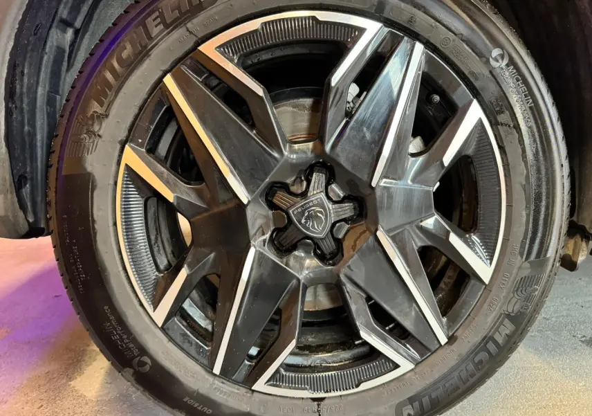 Gros plan sur la jante noire et argentée du Peugeot 5008 1.2 HYBRID 136 GT gris avec logo central lion.