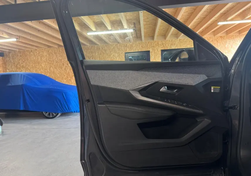Vue intérieure de la porte avant gauche grise du Peugeot 5008 1.2 Hybrid 136 GT avec habillage tissu et plastique noir.
