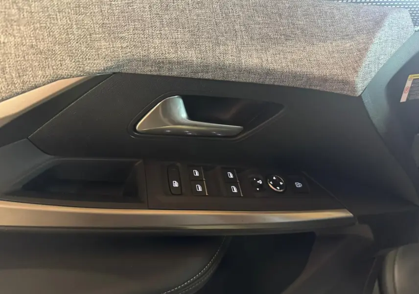Gros plan sur la garniture de porte côté gauche du Peugeot 5008 gris, avec commandes électriques et poignée argentée.