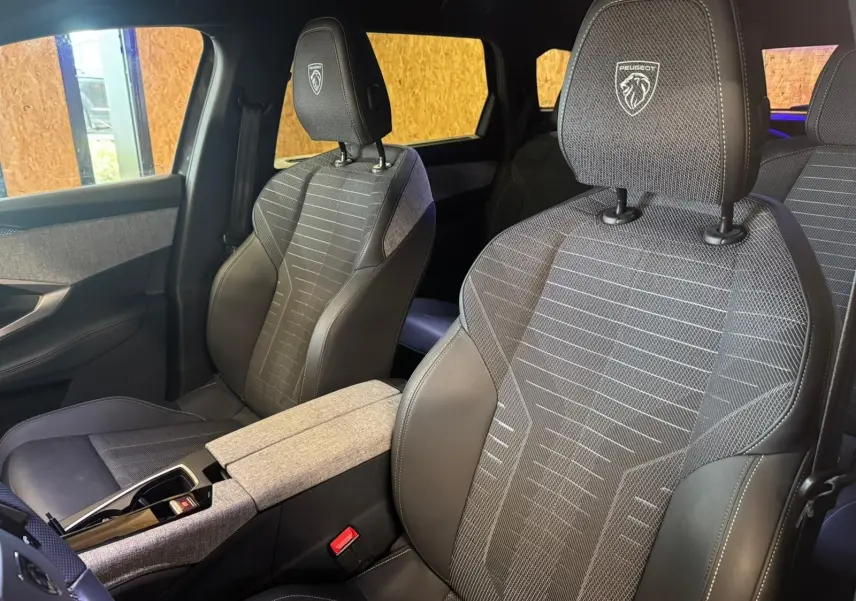 Vue intérieure rapprochée des sièges avant gris tissu et cuir du Peugeot 5008 1.2 HYBRID 136 GT avec logo brodé sur les appuie-têtes.