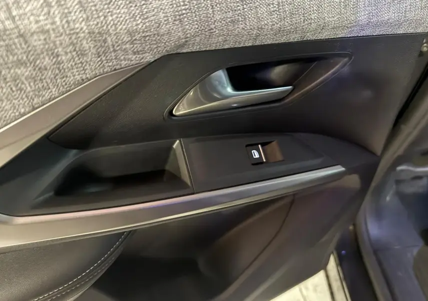 Gros plan sur la poignée intérieure et le bouton de verrouillage de la porte côté gauche d’un Peugeot 5008 gris.