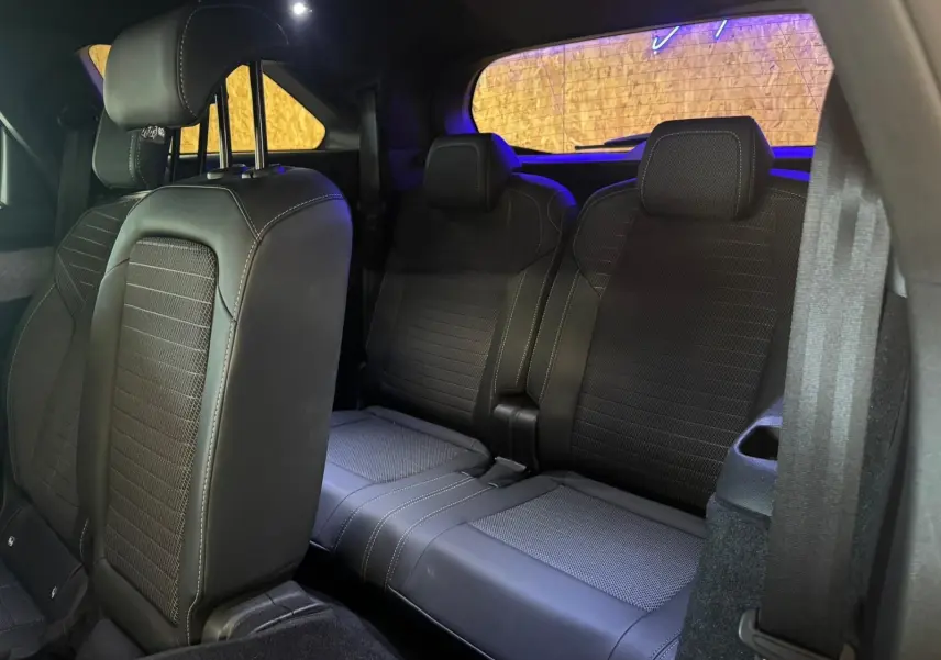 Vue intérieure arrière du Peugeot 5008 1.2 HYBRID 136 GT, sièges tissu noir avec surpiqûres blanches, ambiance tamisée.