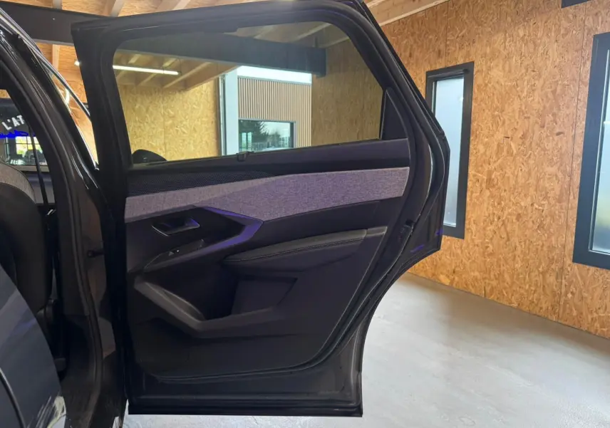 Vue intérieure sur la porte arrière gauche ouverte d’un Peugeot 5008 gris 1.2 Hybrid 136 GT avec habillage tissu gris et noir.