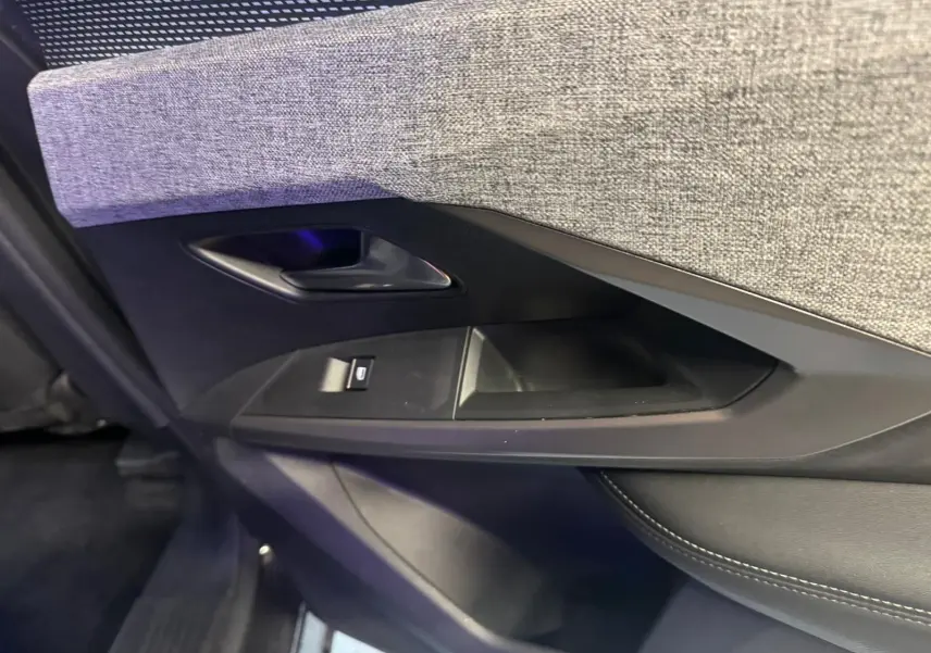 Gros plan sur la garniture intérieure de la porte côté gauche du Peugeot 5008 gris, avec tissu gris et commande de fenêtre.