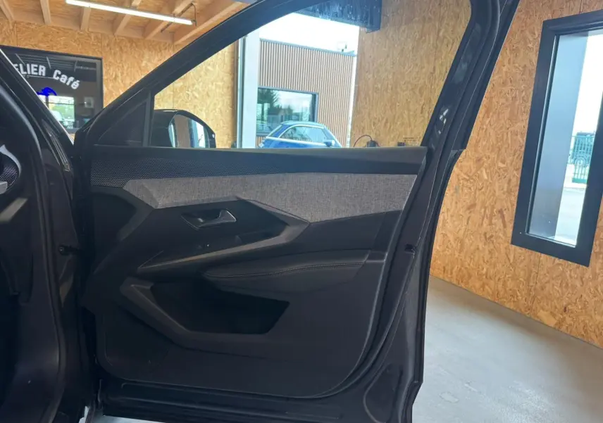Vue intérieure de la porte avant gauche du Peugeot 5008 gris 2025, avec garniture tissu et plastique noir.