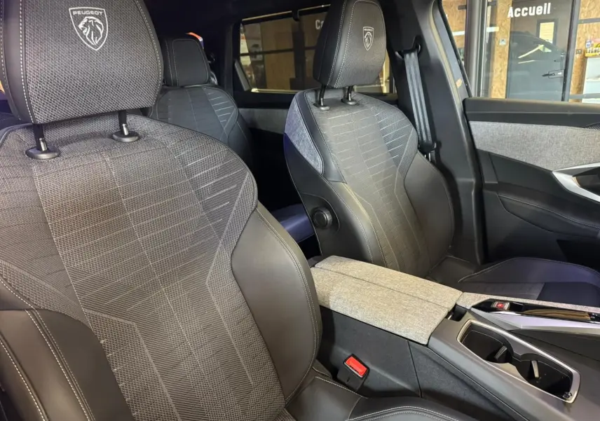 Vue intérieure rapprochée des sièges avant gris tissu et cuir du Peugeot 5008 1.2 HYBRID 136 GT avec logo sur appuie-tête.