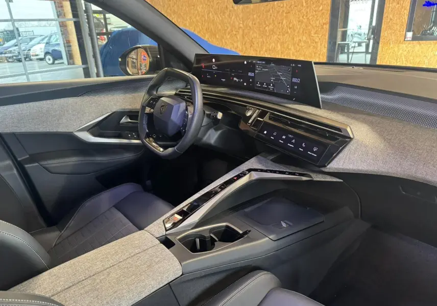 Vue intérieure côté conducteur du Peugeot 5008 1.2 Hybrid 136 GT 2025 avec tableau de bord numérique et habillage gris tissu.