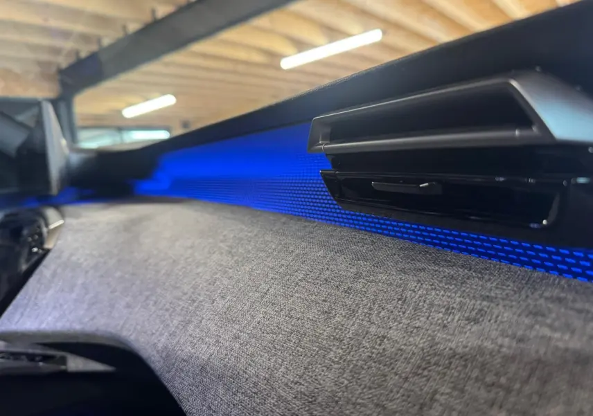 Détail intérieur du tableau de bord du Peugeot 5008 gris 1.2 HYBRID 136 GT avec éclairage d’ambiance bleu.