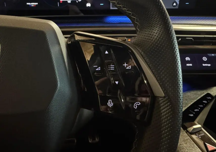 Gros plan sur les commandes au volant à droite du Peugeot 5008 gris 2025, avec tableau de bord digital en arrière-plan.