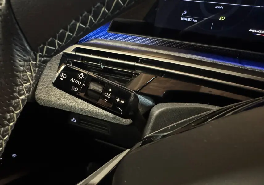 Gros plan sur la commande des feux et clignotants côté gauche du tableau de bord noir du Peugeot 5008 gris 1.2 Hybrid 136 GT.