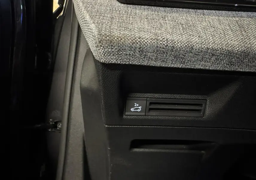 Gros plan sur le bouton d'ouverture du coffre dans l'habitacle du Peugeot 5008 gris, tissu intérieur gris clair.