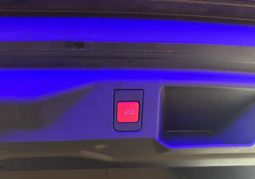 Bouton rouge d'ouverture électrique du coffre sur la plage arrière d'un Peugeot 5008 gris 1.2 Hybrid 136 GT 2025.