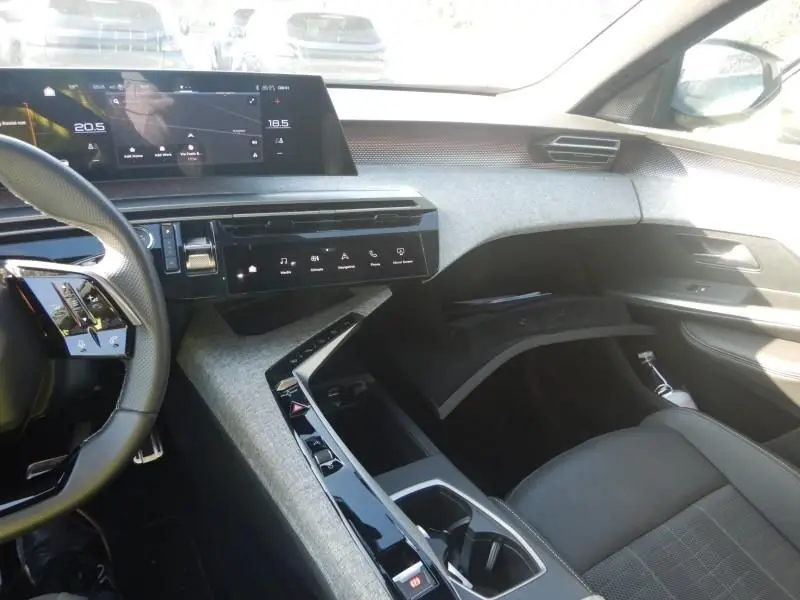 Vue intérieure côté passager du tableau de bord et console centrale du Peugeot 5008 gris hybride avec écran tactile et volant partiel visible.