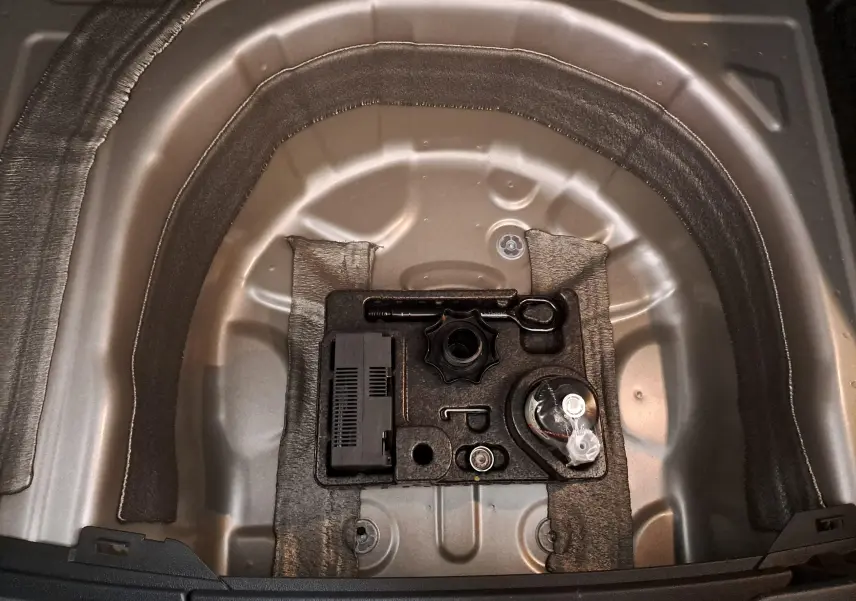 Vue rapprochée du coffre ouvert d’un Volkswagen Taigo 2025 argent, montrant le rangement pour outils sous le plancher.