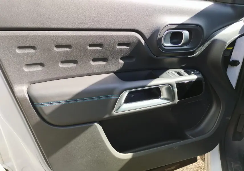 Vue intérieure côté gauche de la porte avant blanche nacrée du Citroën C5 Aircross avec poignée argent et surpiqûres bleues.