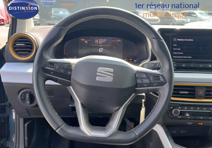 Vue intérieure centrée sur le volant du SEAT Arona 2025, avec tableau de bord numérique et détails orange autour des aérateurs.