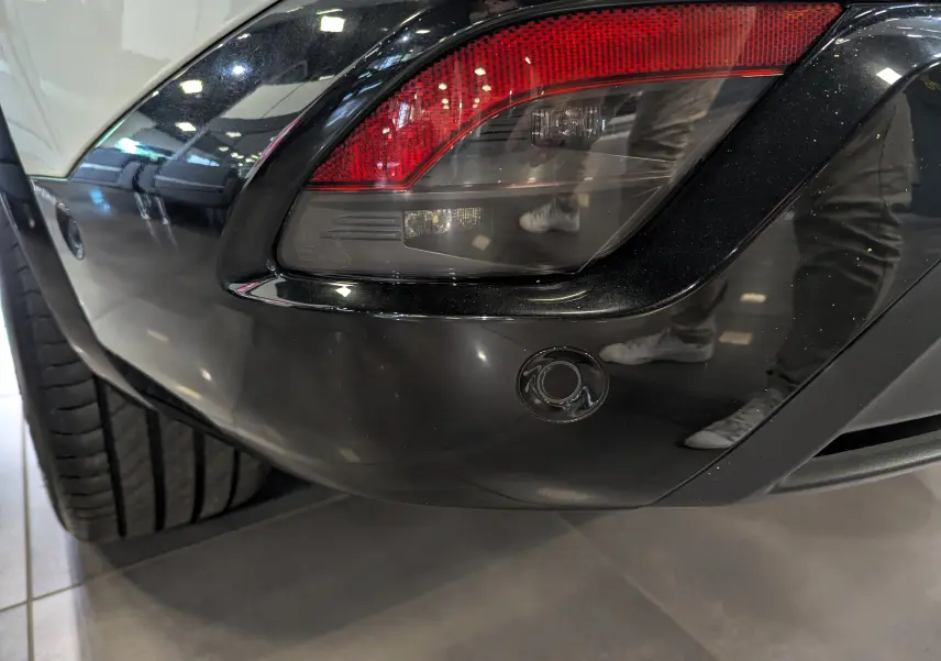 Gros plan sur le feu arrière droit noir brillant du Renault Austral blanc nacré avec pare-chocs noir et capteur de recul.