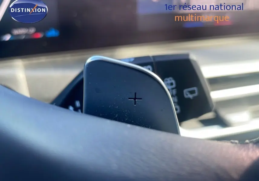 Gros plan sur la palette de changement de vitesse "+" derrière le volant d'une BMW Série 3 Touring noire, intérieur moderne.