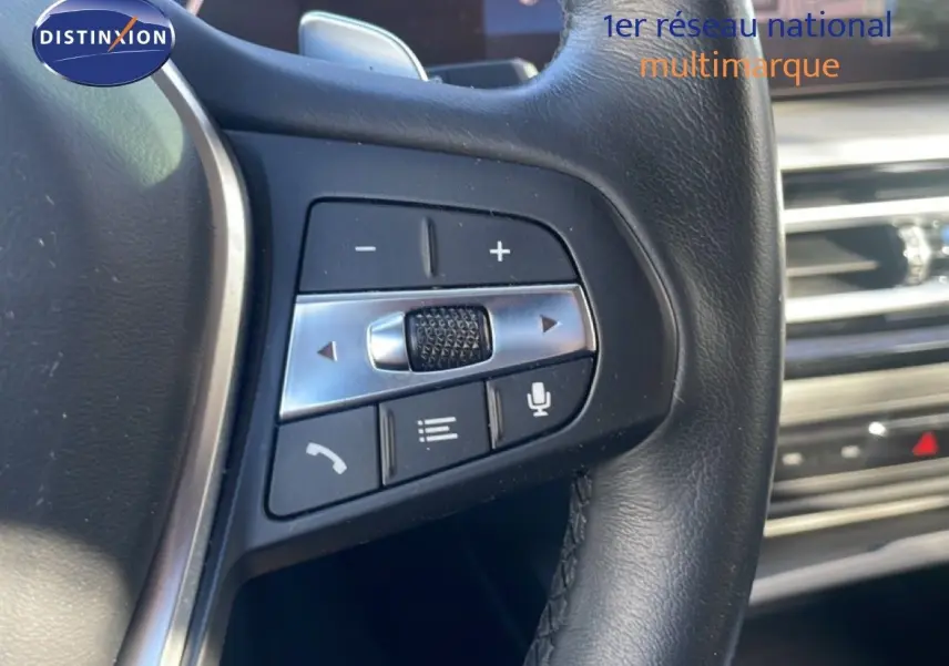 Gros plan sur les commandes du volant en cuir noir de la BMW Série 3 Touring F31 noir saphir, avec tableau de bord en arrière-plan.