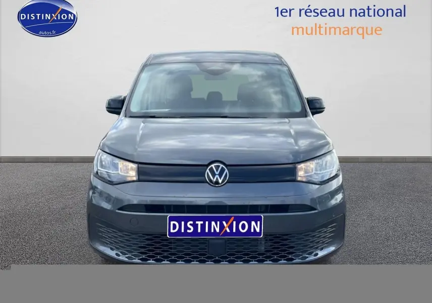 Vue frontale d'un Volkswagen Caddy gris indien 2025 avec calandre noire et phares allumés.