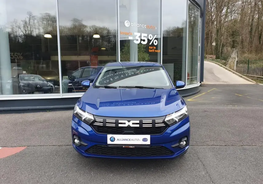 Vue avant d'une Dacia Sandero 2025 bleu Iron avec signature lumineuse LED et feux antibrouillard, stationnée devant un bâtiment.