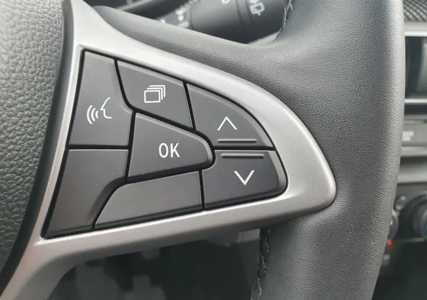 Gros plan sur les commandes multifonctions à gauche du volant en cuir noir de la Dacia Sandero 2025.
