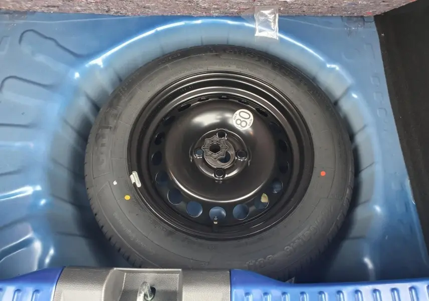 Gros plan sur la roue de secours noire dans le coffre bleu Iron d'une Dacia Sandero 2025.