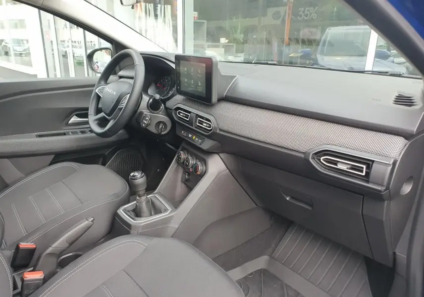Intérieur de la Dacia Sandero 2025 vu côté passager, avec tableau de bord moderne et siège tissu gris.