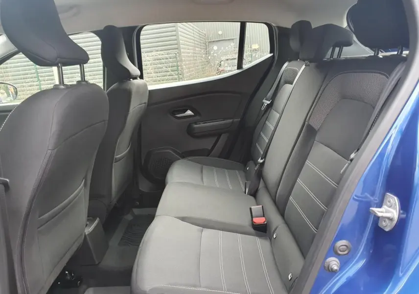 Vue intérieure côté arrière droit de la Dacia Sandero 2025 bleu Iron, montrant la banquette arrière en tissu gris.