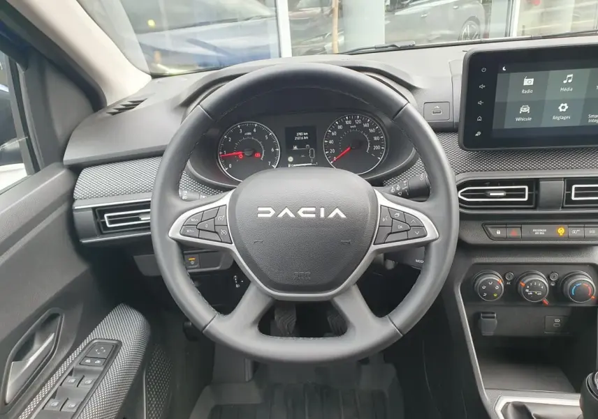 Vue intérieure centrée sur le volant noir de la Dacia Sandero 2025 avec tableau de bord et écran tactile.