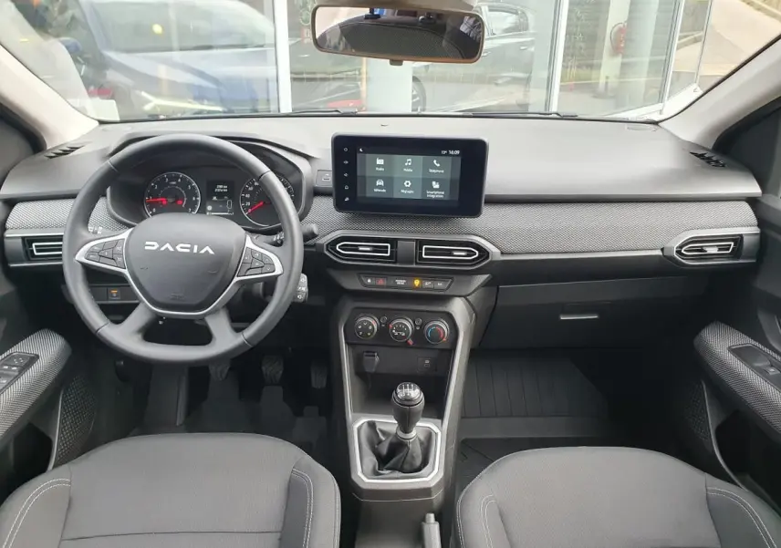 Vue intérieure avant du tableau de bord et volant noir de la Dacia Sandero 2025 avec écran tactile central et boîte manuelle.