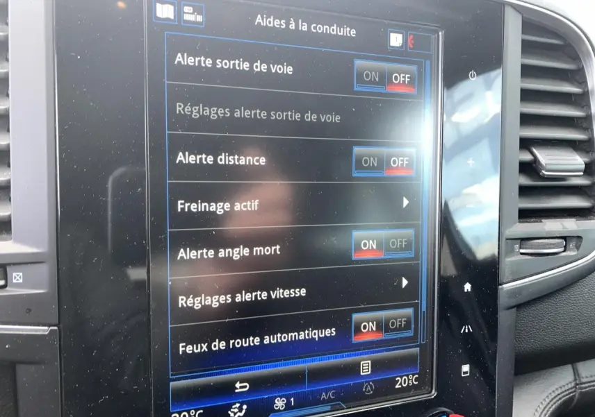 Écran tactile central du Renault Koleos 2019 bleu foncé affichant les aides à la conduite, avec aérateurs latéraux visibles.