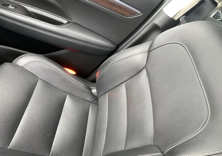 Gros plan sur le siège avant droit en cuir noir avec surpiqûres blanches et insert décoratif bois sur la porte du Renault Koleos.