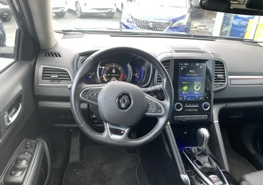 Vue intérieure avant du Renault Koleos 2019, tableau de bord noir avec écran tactile central et volant cuir.