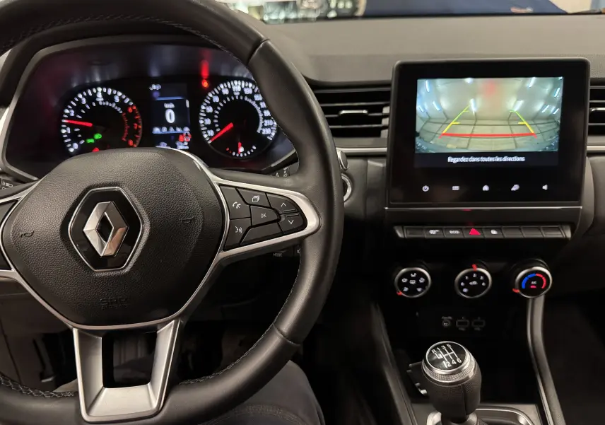 Vue intérieure du tableau de bord du Renault Captur 2021 avec volant, écran de caméra de recul et levier de vitesse manuel.