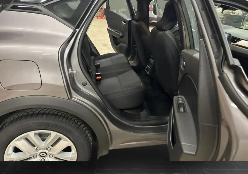 Vue côté gauche arrière du Renault Captur gris foncé avec porte arrière ouverte, montrant l'intérieur noir des sièges arrière.