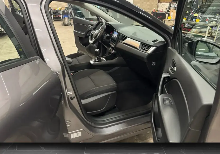 Vue intérieure côté conducteur d’un Renault Captur gris foncé avec tableau de bord noir et volant multifonction.