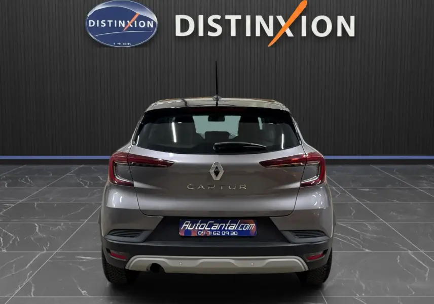 Vue arrière d’un Renault Captur gris foncé avec toit noir, stationné en intérieur devant un mur noir marqué Distinxion.