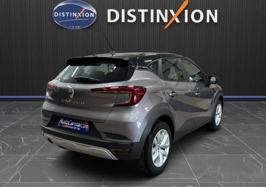 Vue 3/4 arrière droite du Renault Captur gris foncé avec toit noir, en intérieur sur sol carrelé, logo Distinxion en arrière-plan.
