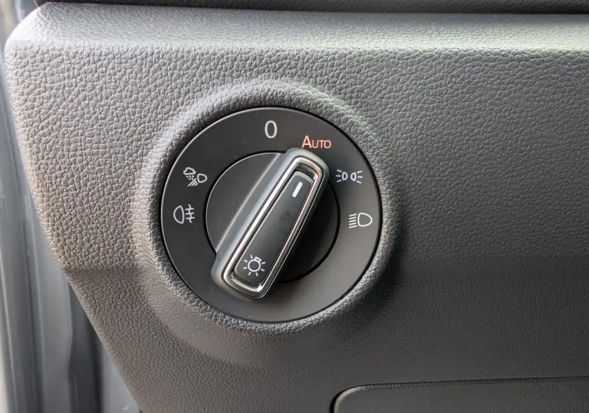 Gros plan sur le bouton de commande des phares du Volkswagen T-Roc gris, situé côté gauche du tableau de bord.