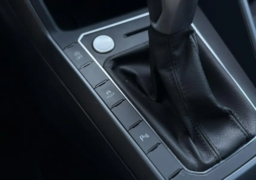 Gros plan sur la console centrale noire du Volkswagen Taigo TSI 116 DSG R-Line, avec levier de vitesse cuir et boutons de contrôle.