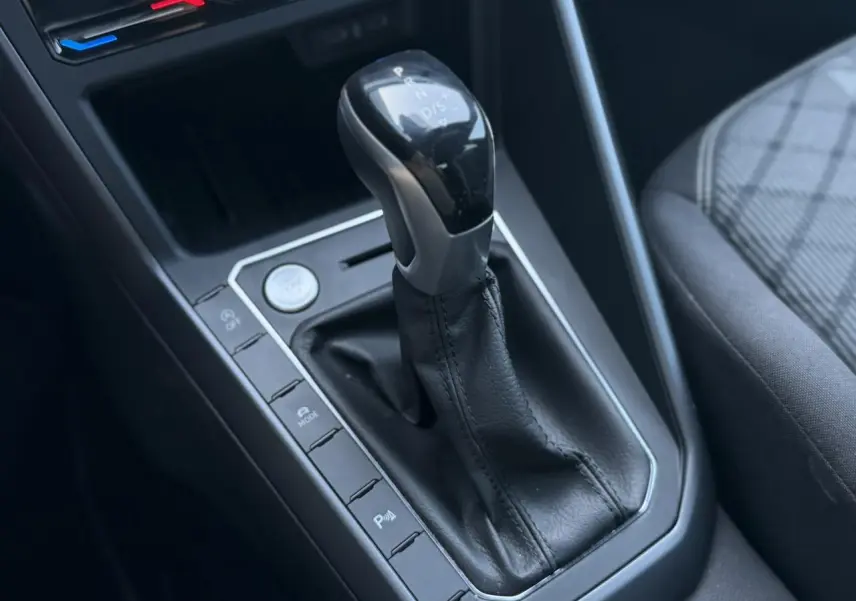 Gros plan sur la console centrale du Volkswagen Taigo gris intense, mettant en valeur le levier de vitesse automatique et les commandes adjacentes.