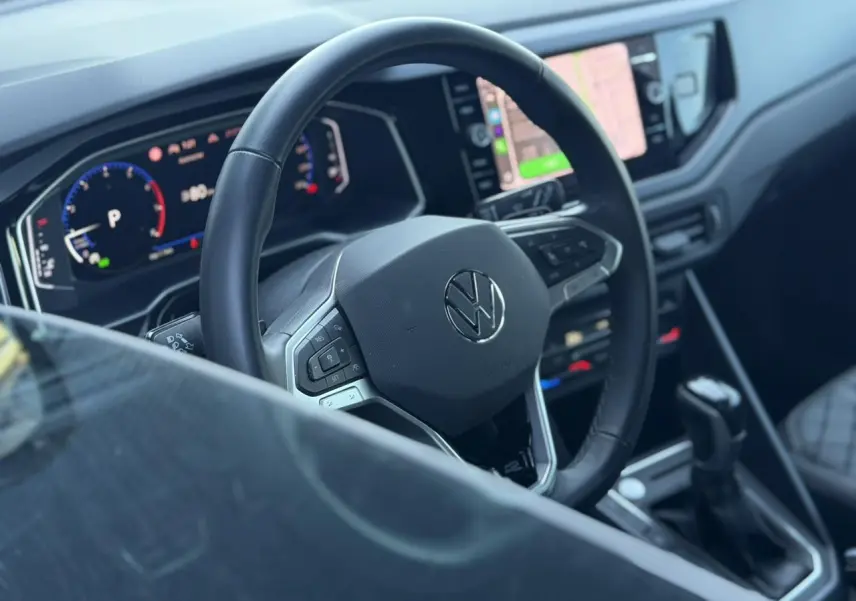 Vue intérieure centrée sur le volant multifonctions cuir Volkswagen, avec tableau de bord numérique et écran tactile visible.