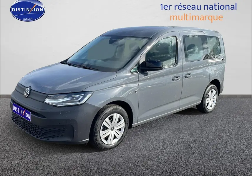 Volkswagen Caddy gris pur en 3/4 avant droit, avec barres de toit et jantes alliage visibles.