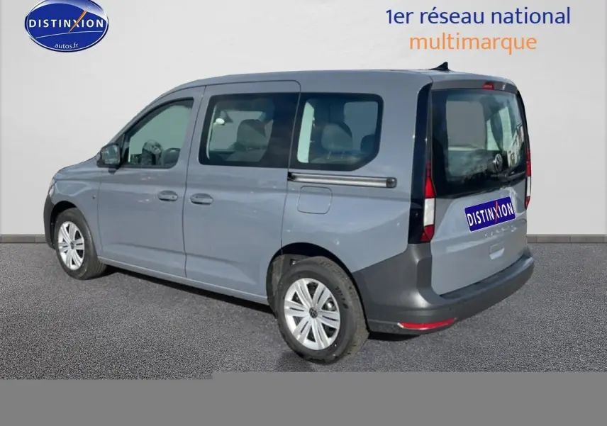 Vue 3/4 arrière droite d'un Volkswagen Caddy gris pur avec vitres teintées et barres de toit noires.